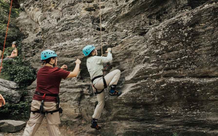 a student rock climbs while another spots them on a rock climbing trip in north carolina